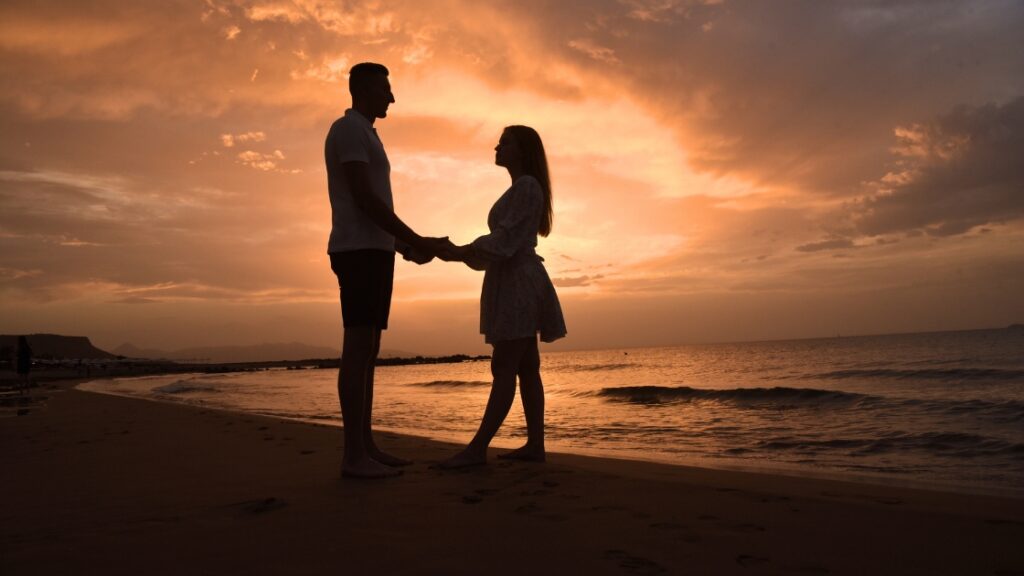 Silhouette of a couple holding hands on the beach during a golden sunset.