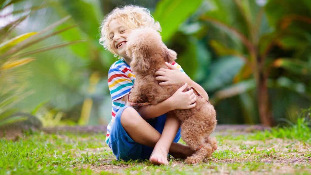 Smiling boy hugging a brown puppy in a green garden, enjoying a candid outdoor moment.