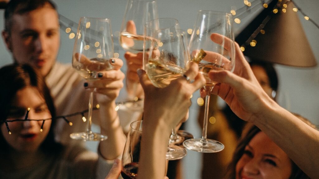 Group of people raising glasses for a toast at a festive celebration with warm lights in the background.