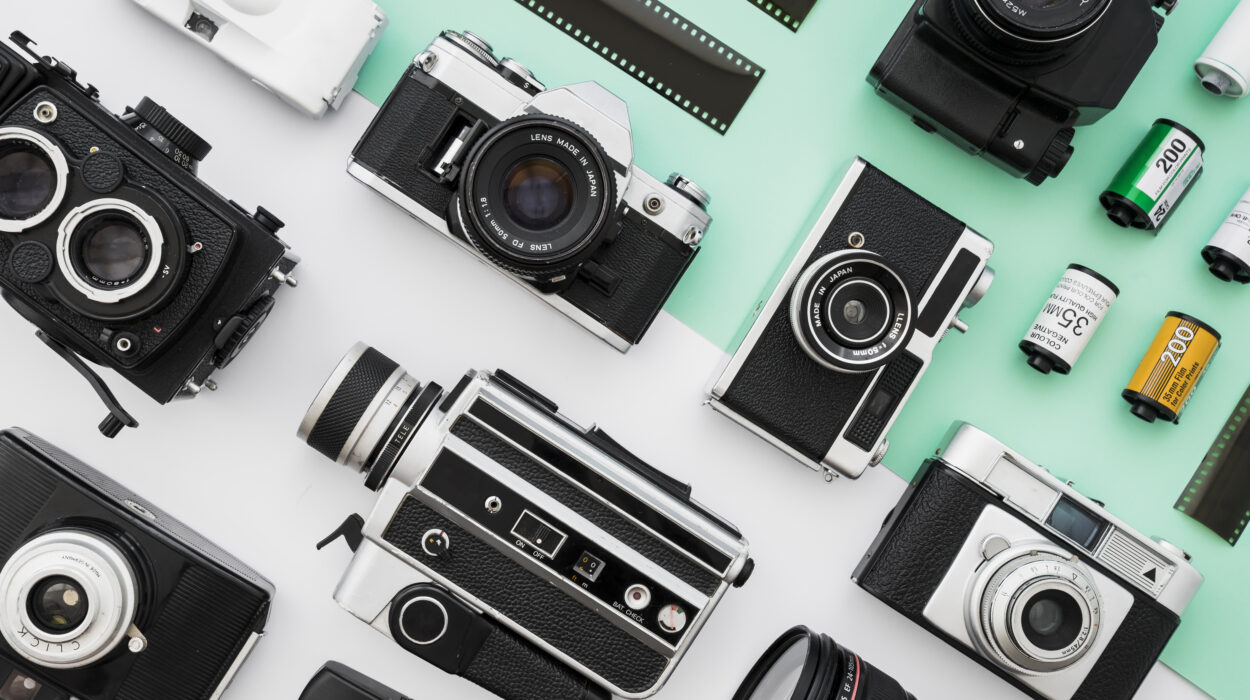 Collection of vintage photo and video cameras on a teal background, with film rolls nearby.