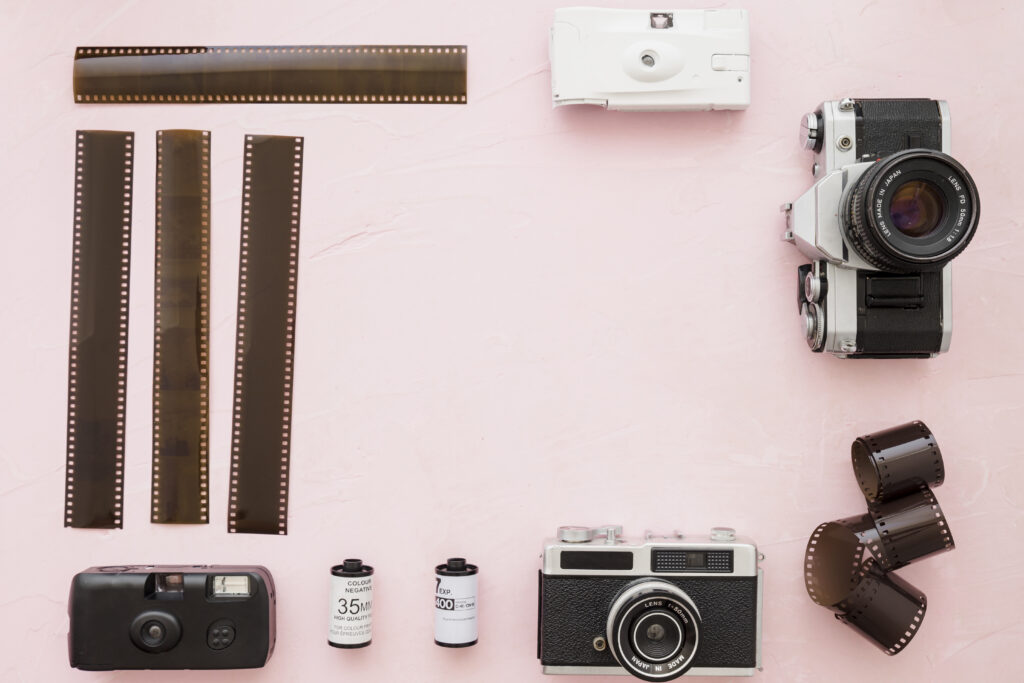 Vintage film cameras on a pink background, arranged with photography tools.